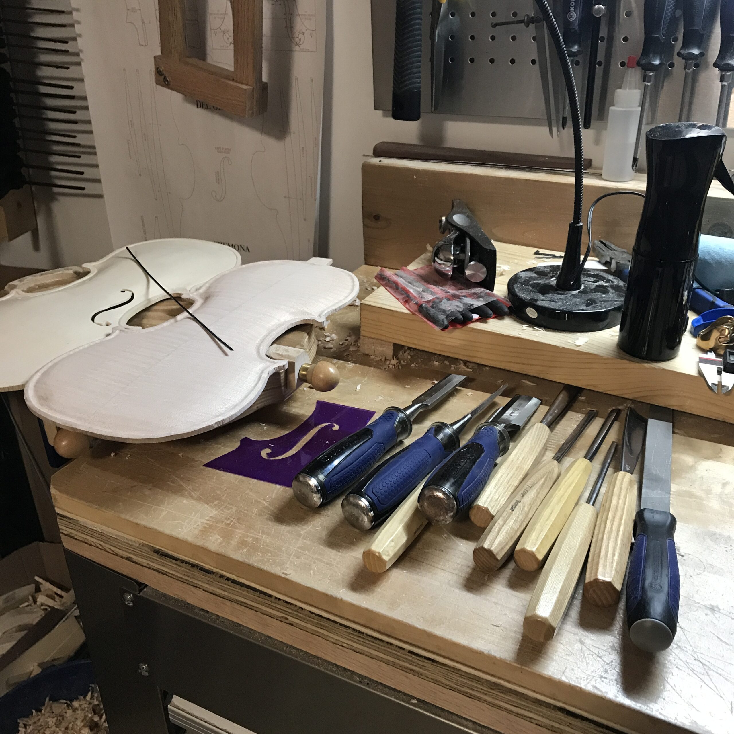 A workbench with chisels, gouges, a violin top and violin bottom.