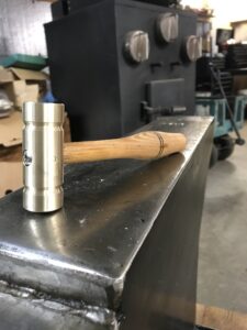 A brass hammer head with wheel spoke handle resting on an anvil